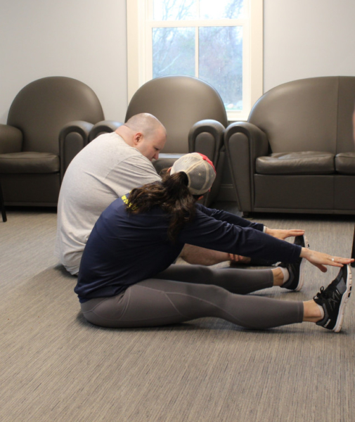 CCV resident and caregiver sitting on the floor working on toe touches